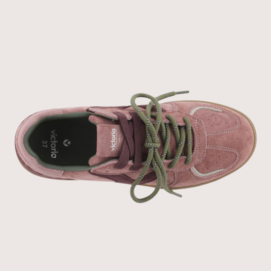 A top-down view of a pink suede sneaker with olive green laces and a black interior, shown on a light beige background.