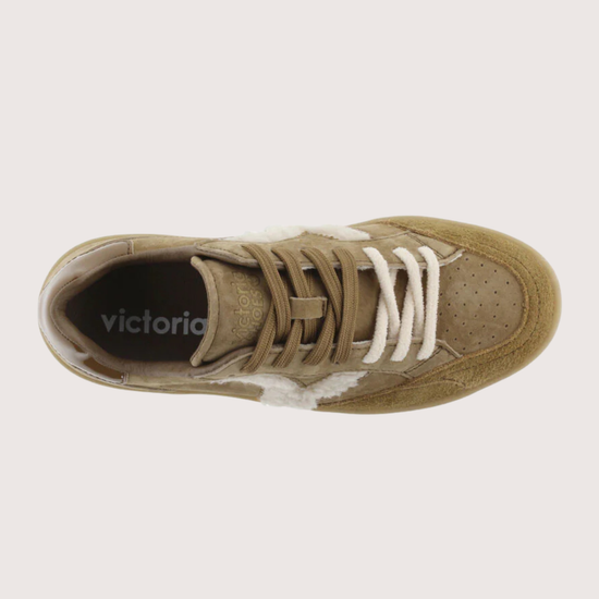 A top-down view of a low-top sneaker in a muted tan/khaki color, featuring white laces and a white side stripe, with the brand name 'victoria' printed on the black insole.