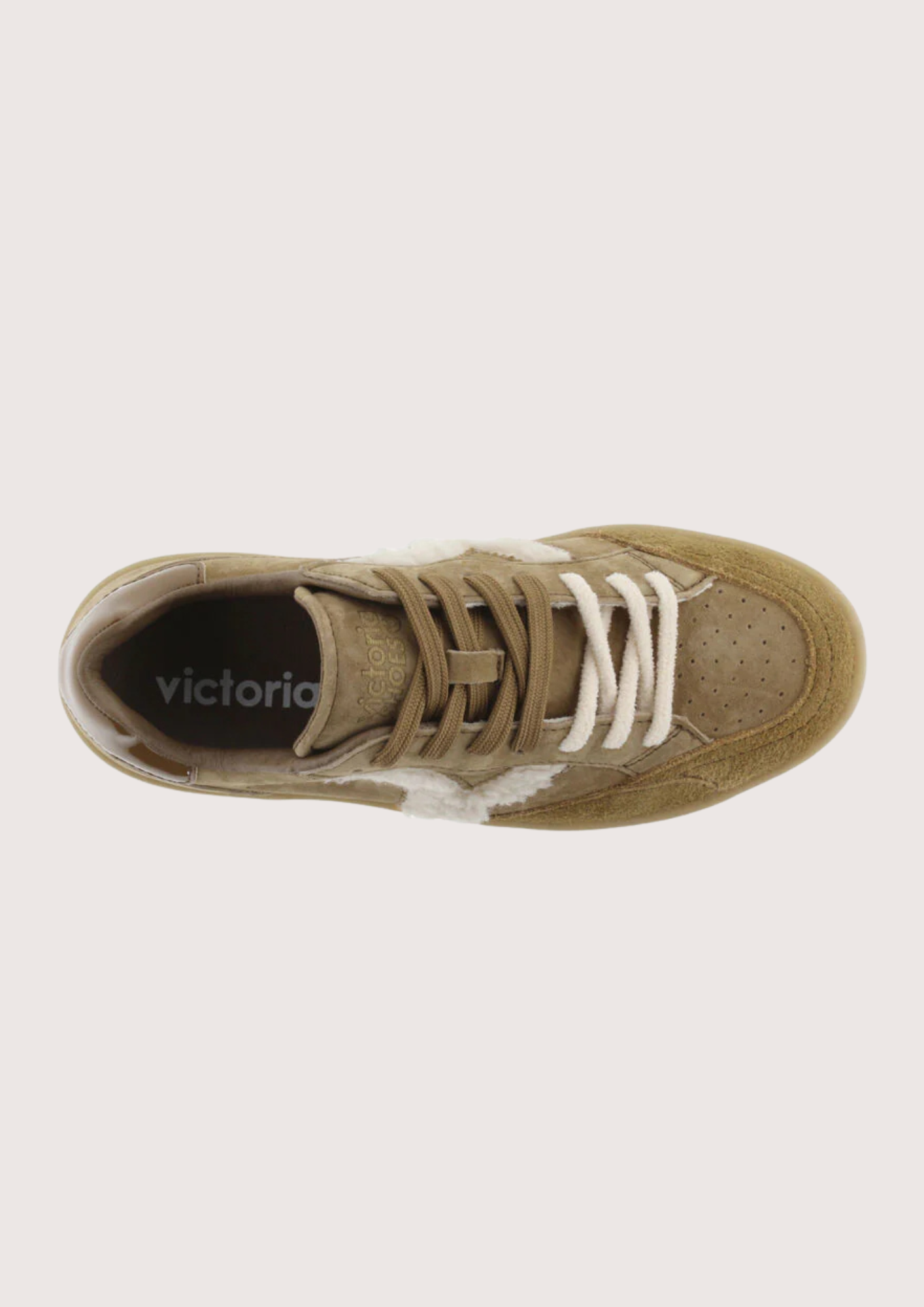 A top-down view of a low-top sneaker in a muted tan/khaki color, featuring white laces and a white side stripe, with the brand name 'victoria' printed on the black insole.