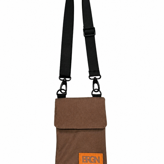 A brown canvas crossbody pouch bag with a black adjustable shoulder strap and a bright orange rectangular logo patch on the front flap. The brand name 'BRGN' is printed in black on the orange patch.