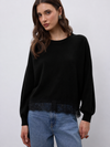 model wearing a black crew neckline knit with lace hem and blue jeans 