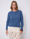 A woman modeling a blue long-sleeve button-front cardigan sweater paired with a cream lace skirt, standing against a plain light gray studio background.