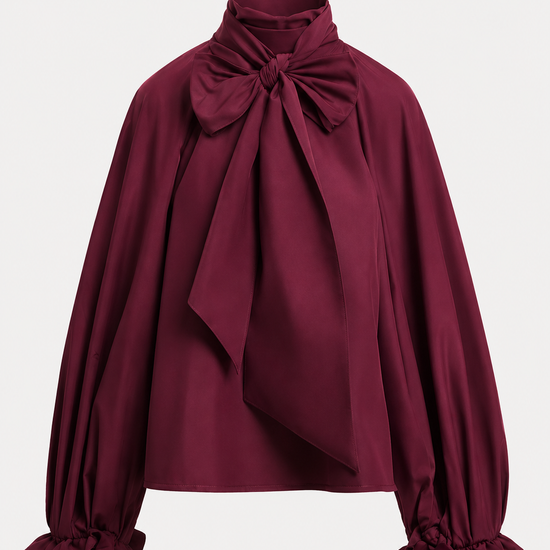 A deep burgundy long-sleeve blouse with a large bow at the high neck, draped front detail, and ruffled cuffs, shown on a light gray background.