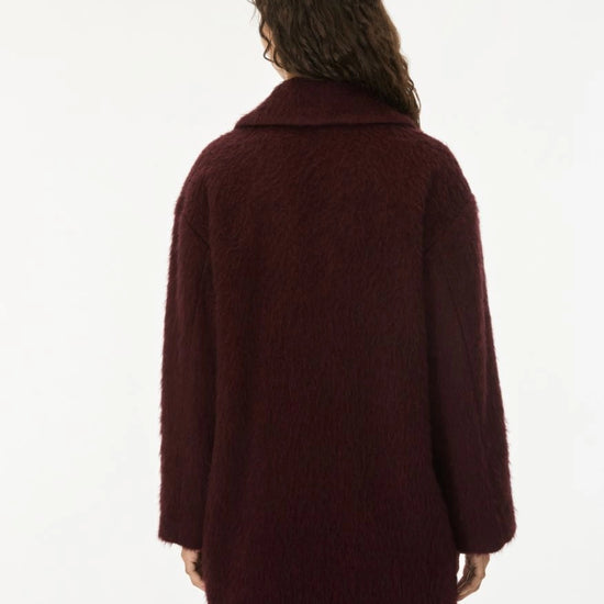 A model shown from the back wearing a textured, fuzzy dark burgundy coat against a plain white background.