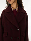 A close-up of a model wearing a dark burgundy fuzzy double-breasted coat over a burgundy top and a patterned collared shirt.