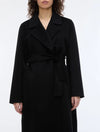 woman wearing A black long coat with a tie belt, shown on a plain light gray background. close up