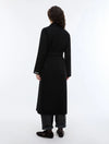 woman wearing a black long coat with a tie belt, shown on a plain light gray background rear view