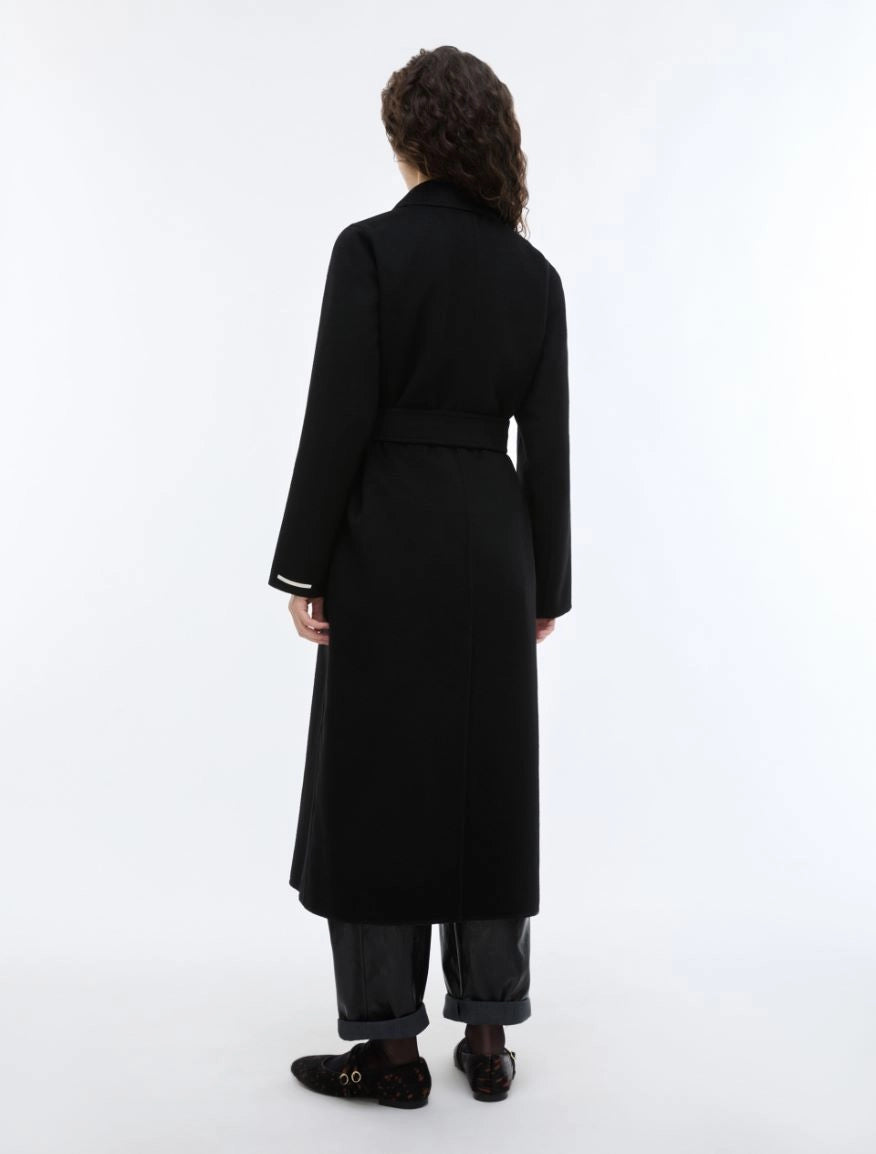 woman wearing a black long coat with a tie belt, shown on a plain light gray background rear view