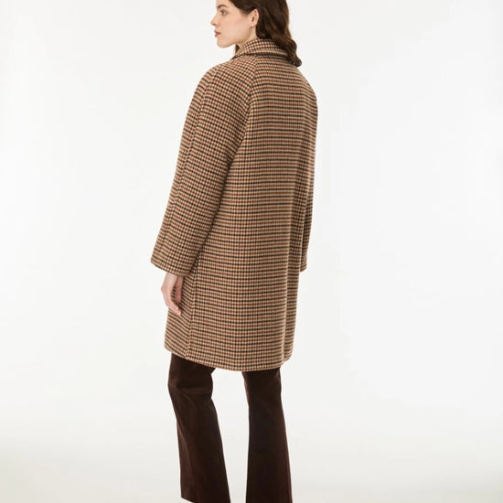 A woman shown from the back wearing a brown and beige houndstooth patterned coat, dark brown cropped trousers, and brown leather block-heel mules, photographed against a clean white studio background.