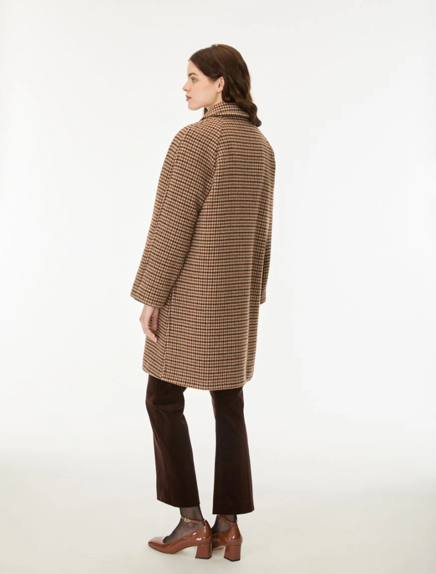 A woman shown from the back wearing a brown and beige houndstooth patterned coat, dark brown cropped trousers, and brown leather block-heel mules, photographed against a clean white studio background.