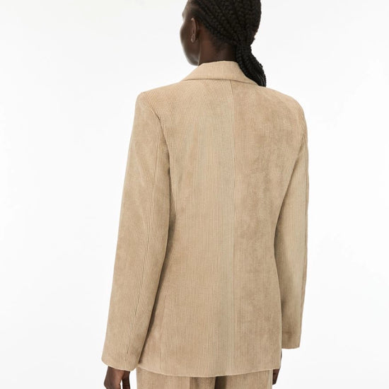 A model shown from the back wearing a light beige corduroy blazer and matching trousers against a plain white studio background.