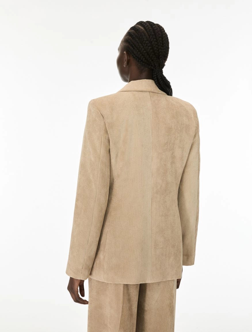 A model shown from the back wearing a light beige corduroy blazer and matching trousers against a plain white studio background.
