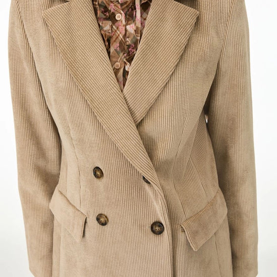 A beige corduroy double-breasted blazer with dark brown buttons, worn over a floral print shirt, shown on a mannequin against a plain white background.