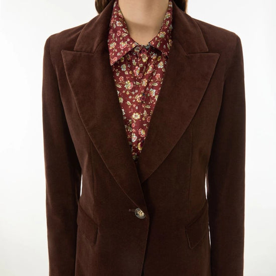 A woman wearing a dark brown suede blazer over a red floral button-down shirt, shown from the chin down against a plain white background.