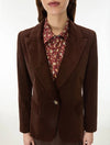 A woman wearing a dark brown suede blazer over a red floral button-down shirt, shown from the chin down against a plain white background.