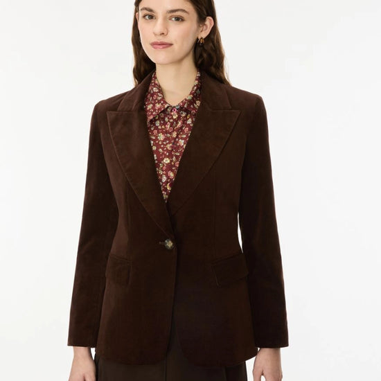 A woman modeling a dark brown corduroy blazer over a patterned collared blouse and dark skirt, photographed against a clean white studio background.
