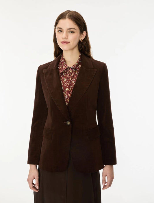 A woman modeling a dark brown corduroy blazer over a patterned collared blouse and dark skirt, photographed against a clean white studio background.