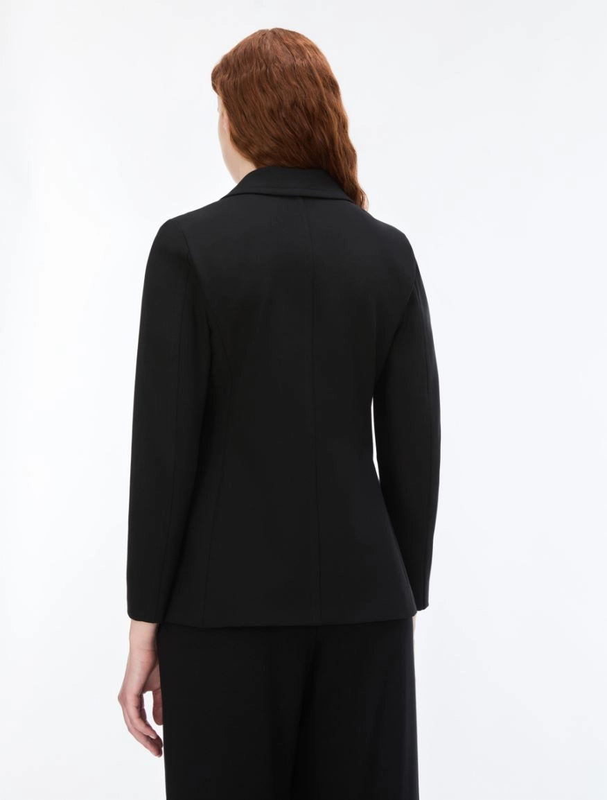 A woman with red hair is shown from the back wearing a black long-sleeve blazer and matching black trousers against a plain white studio background.