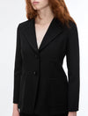 A woman wearing a tailored black blazer with notch lapels, two front buttons, flap pockets, and a structured silhouette, shown against a plain light background.