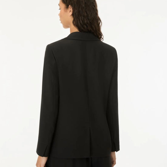 A model shown from the back wearing a black long-sleeve blazer and matching black trousers against a plain white studio background.