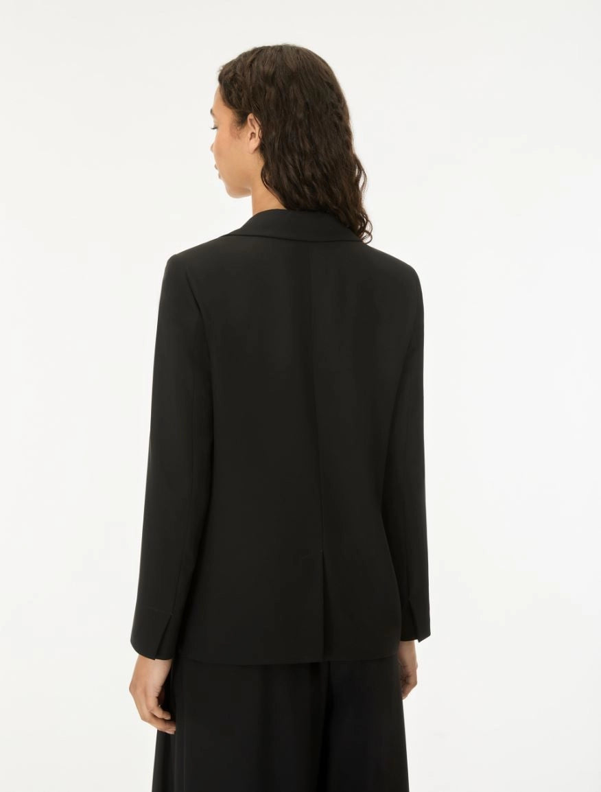 A model shown from the back wearing a black long-sleeve blazer and matching black trousers against a plain white studio background.