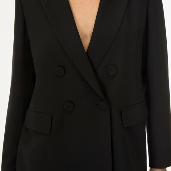 A close-up of a person wearing a black double-breasted blazer with notched lapels and dark buttons, shown against a plain light background.
