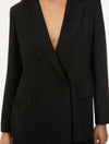 A close-up of a person wearing a black double-breasted blazer with notched lapels and dark buttons, shown against a plain light background.