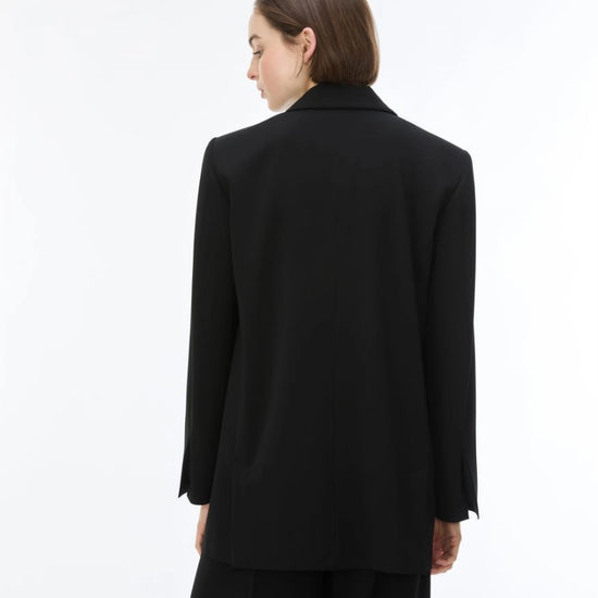 A model shown from the back wearing a black oversized blazer and matching black trousers against a plain white studio background.