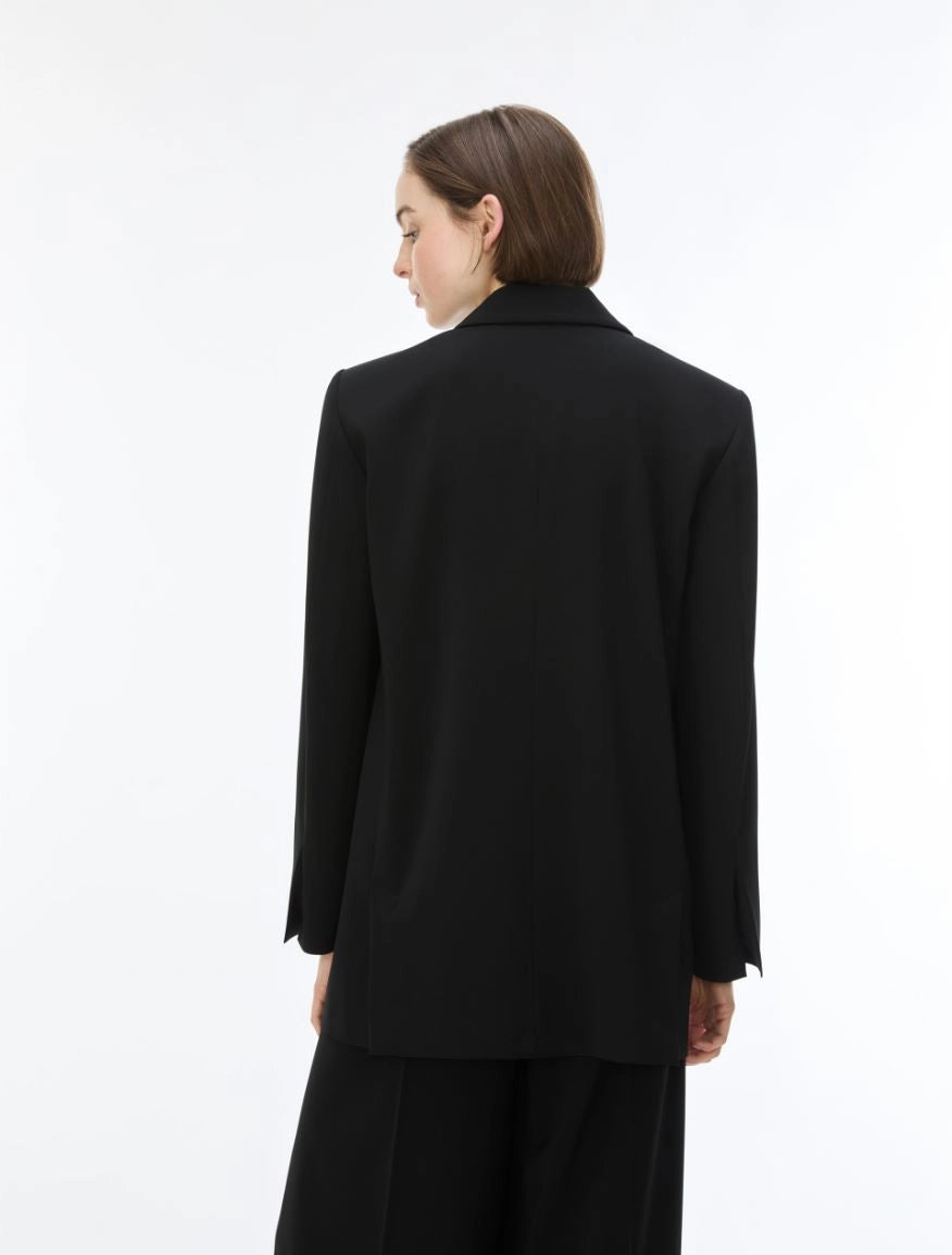 A model shown from the back wearing a black oversized blazer and matching black trousers against a plain white studio background.