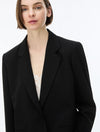 A close-up of a model wearing a black blazer over a white lace top, shot against a plain white background.
