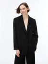 A woman modeling a black tailored blazer with wide lapels, two front buttons, and large patch pockets, paired with black trousers against a clean white studio background.