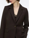 A close-up of a model wearing a dark brown tailored blazer with notch lapels, flap pockets, and a single button closure over a black lace top.