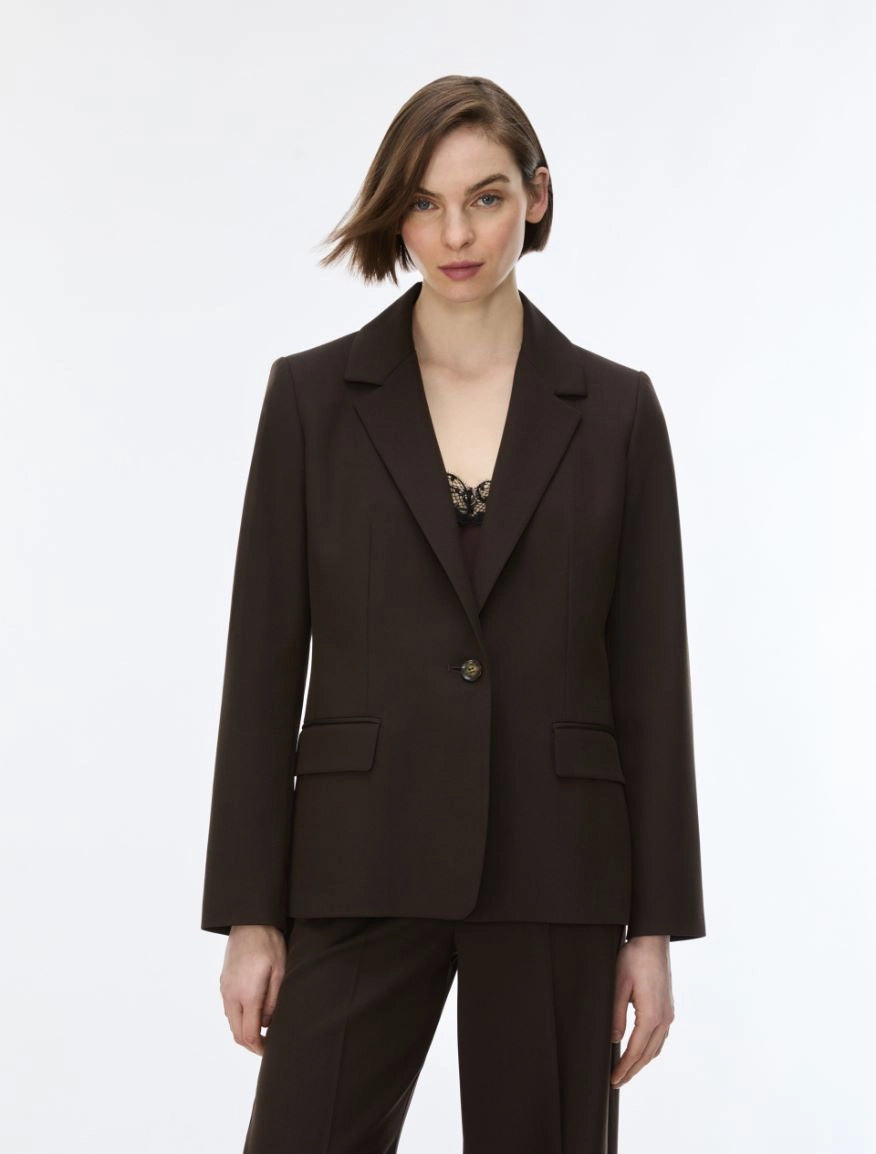 A woman modeling a dark brown tailored blazer with matching trousers against a plain light gray studio background.