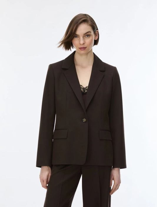 A woman modeling a dark brown tailored blazer with matching trousers against a plain light gray studio background.