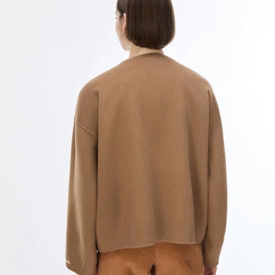 A model shown from the back wearing a camel brown knit cardigan and matching brown trousers against a plain white studio background.
