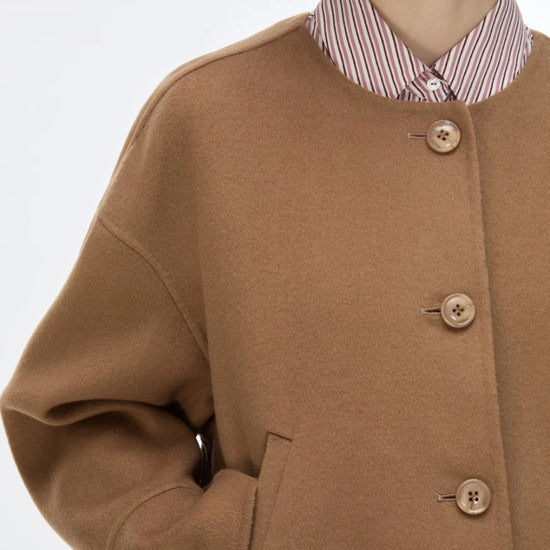 A close-up of a model wearing a camel brown wool-blend coat over a red and white striped collared shirt, against a plain white background.