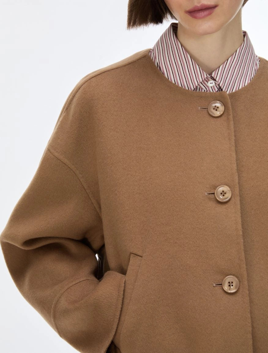 A close-up of a model wearing a camel brown wool-blend coat over a red and white striped collared shirt, against a plain white background.