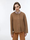 A woman modeling a camel brown cropped button-up cardigan over a striped collared shirt and brown trousers, shot against a plain white studio background.