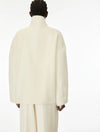 A model shown from the back wearing a voluminous, high-neck cream-colored coat and matching trousers against a plain white studio background.