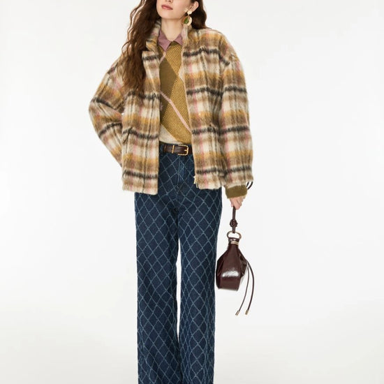 A woman models a stylish outfit featuring a beige and brown plaid fuzzy jacket, a tan knit sweater, dark blue patterned wide-leg trousers, and a small dark brown handbag, set against a plain white studio background.