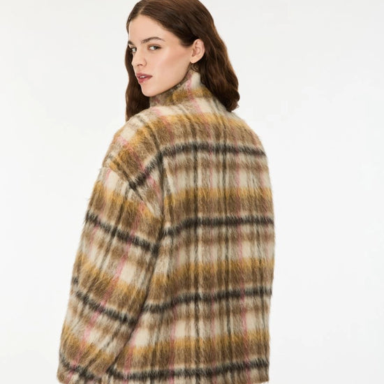 A woman wearing a fuzzy plaid jacket in beige, brown, and black, photographed from the back against a plain white studio background.