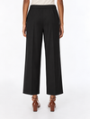 A model shown from the back wearing black wide-leg cropped trousers, a light beige top, and brown leather block-heel mules against a plain white studio background.
