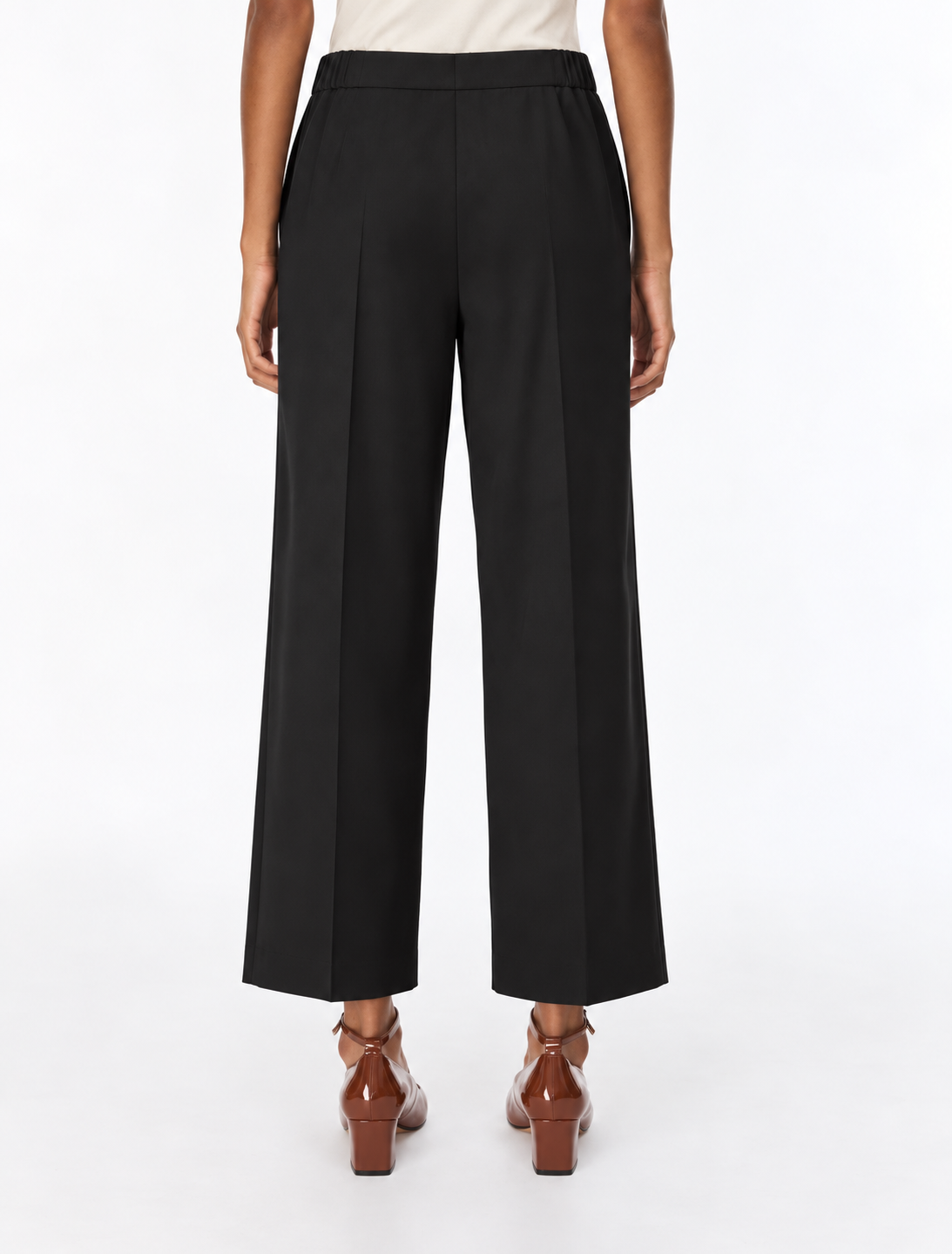 A model shown from the back wearing black wide-leg cropped trousers, a light beige top, and brown leather block-heel mules against a plain white studio background.