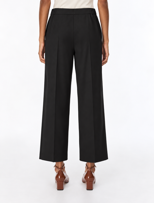 A model shown from the back wearing black wide-leg cropped trousers, a light beige top, and brown leather block-heel mules against a plain white studio background.