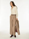 A woman modeling a cream long-sleeve button-up shirt, beige wide-leg plaid trousers, a brown belt, and holding a matching plaid coat, against a plain white studio background.