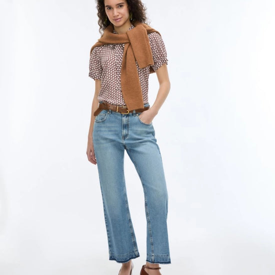 woman wearing geometric blouse with neck tie and jeans on white background