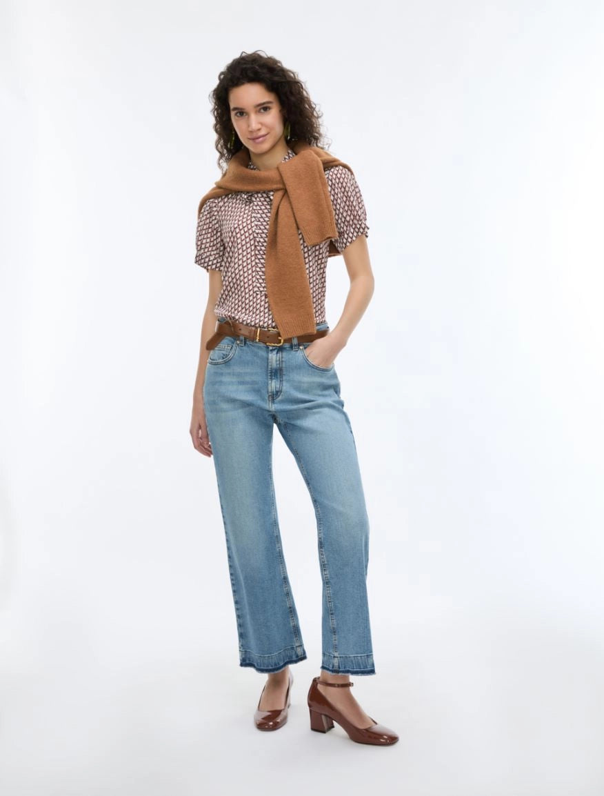woman wearing geometric blouse with neck tie and jeans on white background