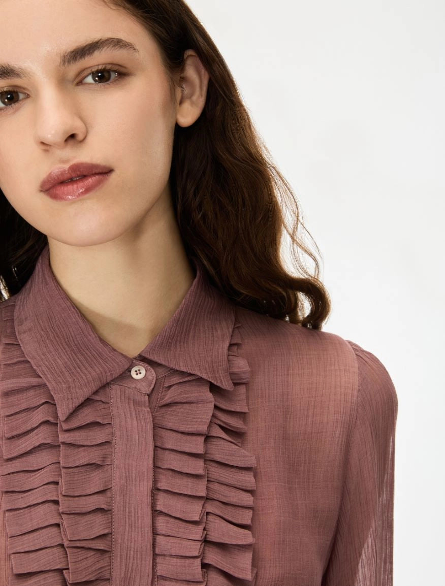 Close-up of a woman wearing a dusty rose ruffled blouse with a pointed collar and button placket, photographed against a clean white background.