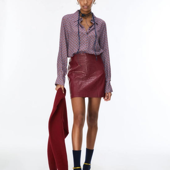 woman wearing a blue and red pattern shirt and red skirt holding a red jacket on a white background