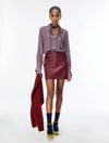 woman wearing a blue and red pattern shirt and red skirt holding a red jacket on a white background